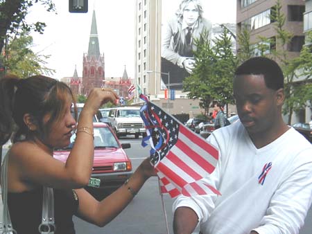A man and woman attach a flag to a car antenna.